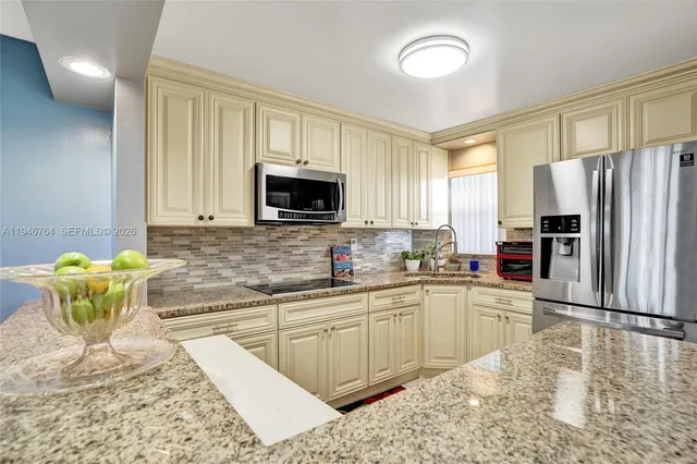 a kitchen with stainless steel appliances granite countertop a sink a stove a refrigerator a window with white cabinets and wooden floor