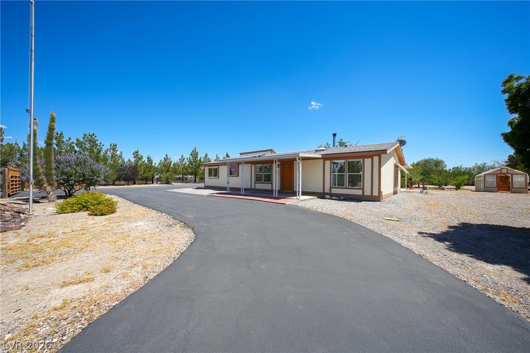1831 West Horn Road Pahrump, NV 89048 - Photo 29 of 59 A lengthy paved driveway leads to a single-story residence with a covered entryway and surrounding gravel landscaping.