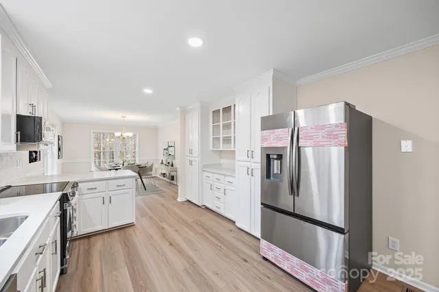 a large kitchen with a refrigerator a sink dishwasher a stove and white cabinets with wooden floor