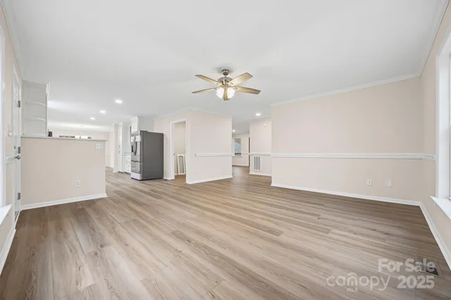 a view of an empty room with wooden floor and a ceiling fan