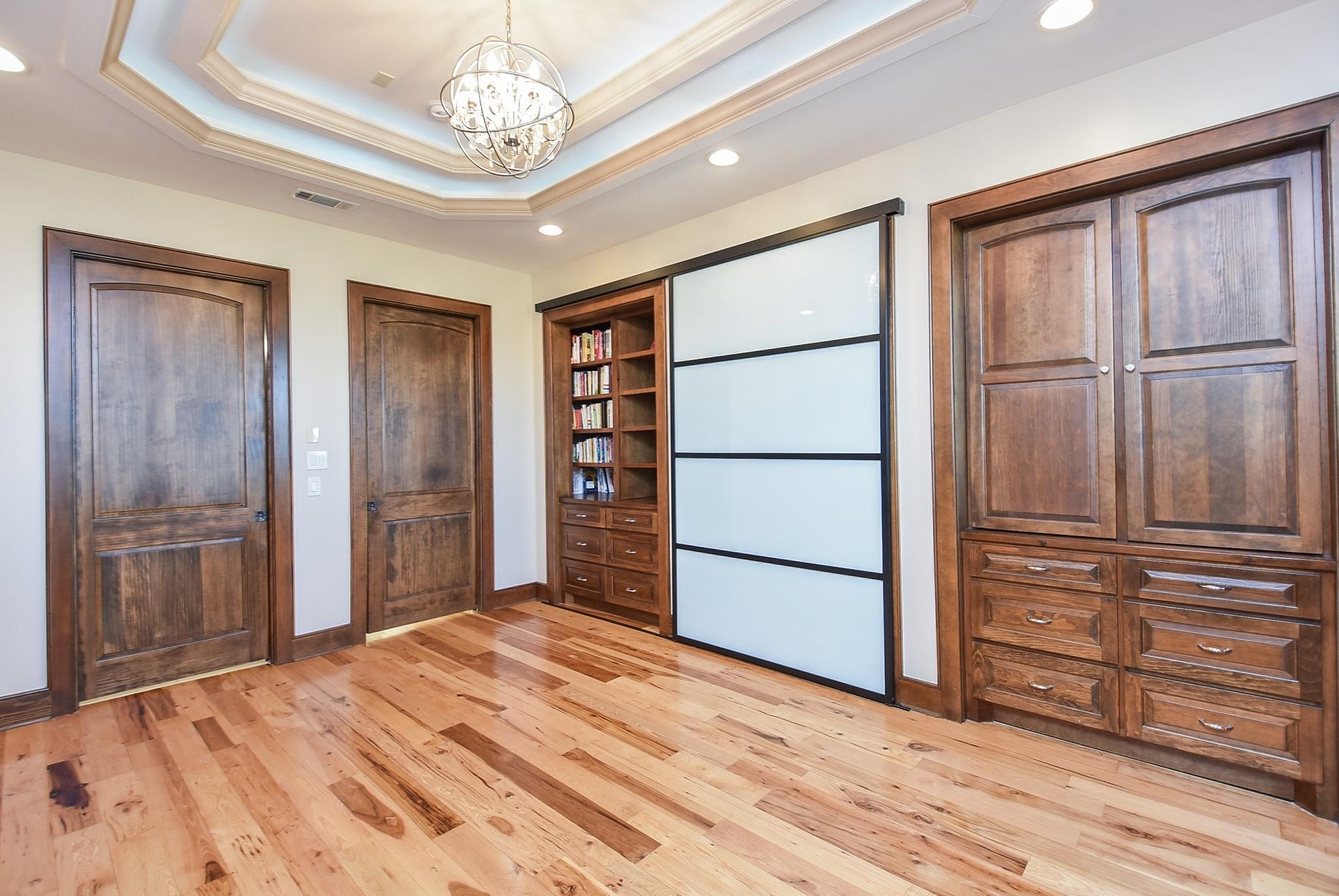 825 Grubbs Road Sealy, TX 77474 - Photo 21 of 47 This room features elegant wood flooring and rich wooden doors, with built-in shelving and modern frosted sliding panels. A tray ceiling with recessed lighting and a chandelier adds a touch of sophistication. Ideal for a study or library.