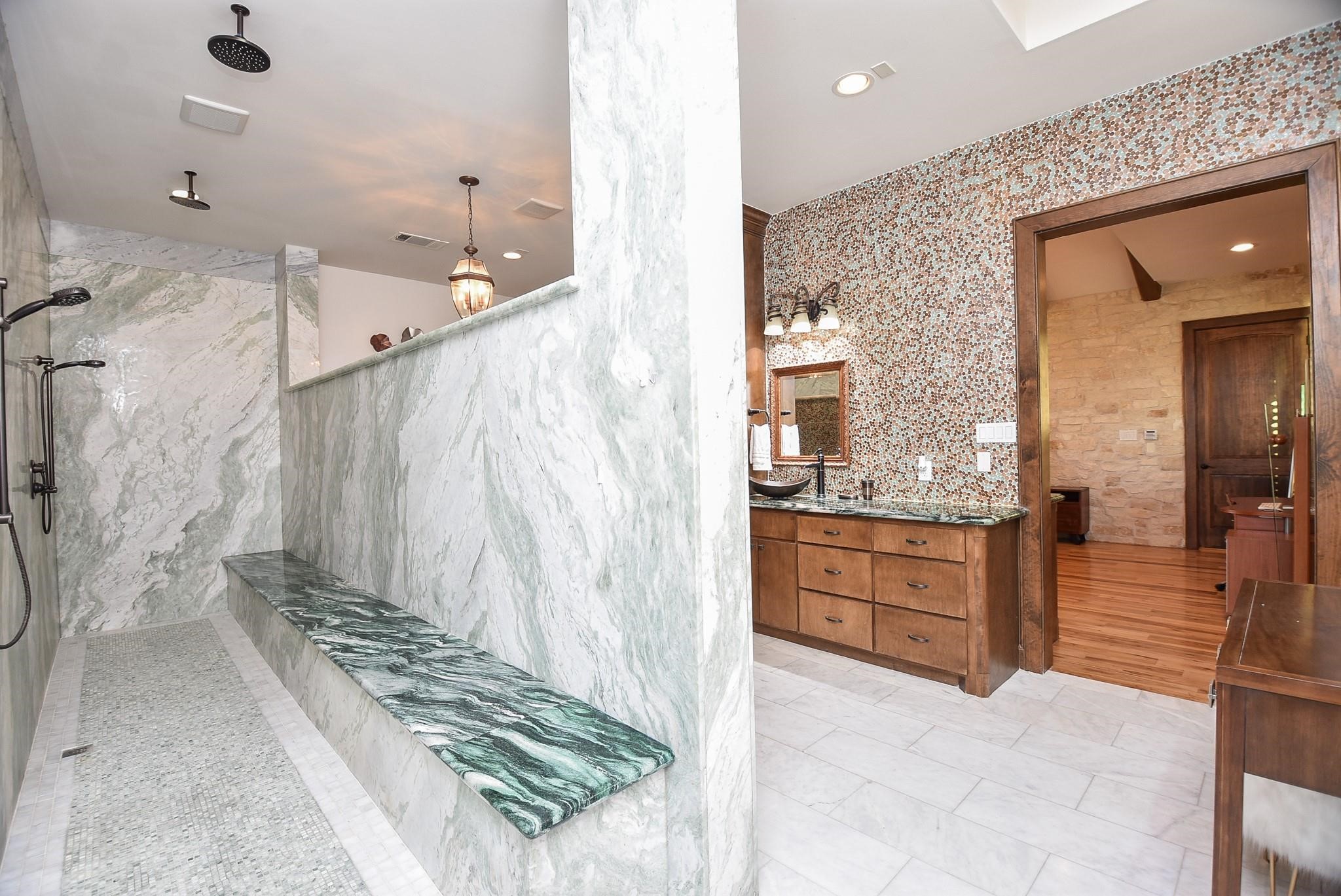 825 Grubbs Road Sealy, TX 77474 - Photo 33 of 47 This bathroom features a spacious, luxurious shower with marble walls and a long bench, complemented by a stylish vanity area with dual sinks and a textured accent wall. The space combines elegance with functionality, perfect for a serene retreat.