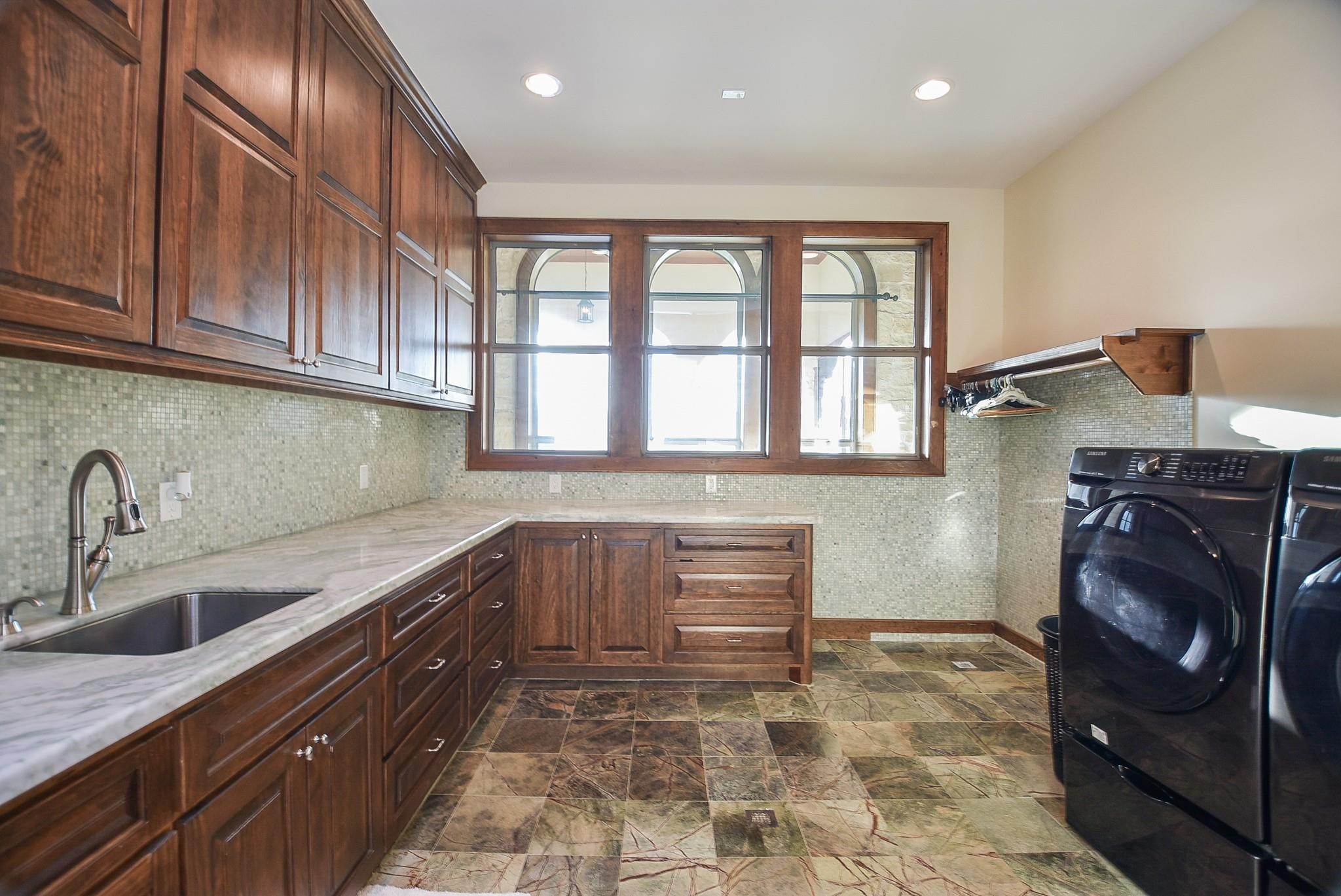 825 Grubbs Road Sealy, TX 77474 - Photo 37 of 47 This spacious laundry room features elegant wood cabinetry, a modern sink, and ample counter space. It includes a sleek washer and dryer set, large windows for natural light, and stylish tiled flooring.