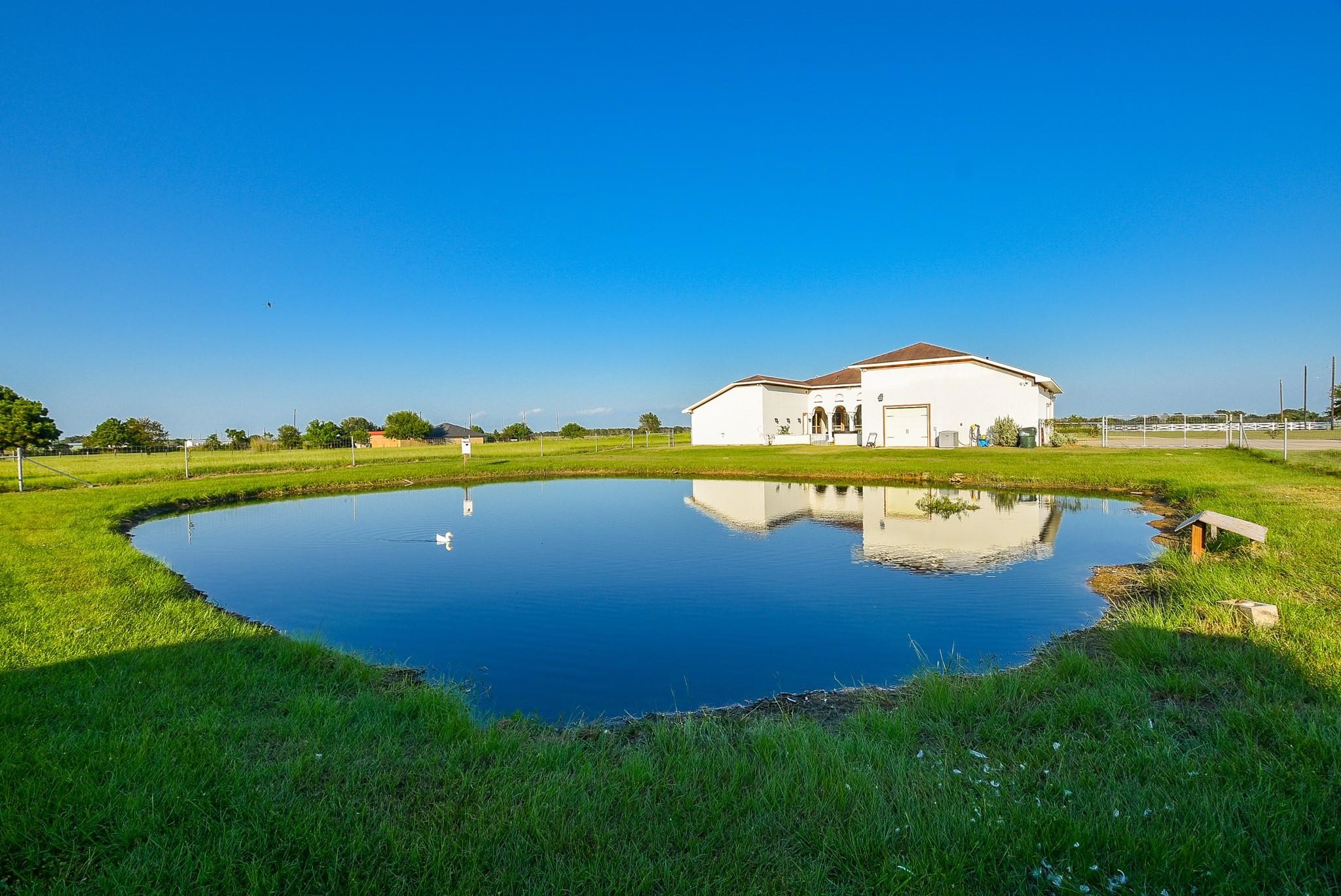 825 Grubbs Road Sealy, TX 77474 - Photo 47 of 47 This property features a charming home with a beautiful pond in the foreground, surrounded by lush greenery. The house is set in a spacious, open area, offering peaceful rural views and a serene atmosphere.