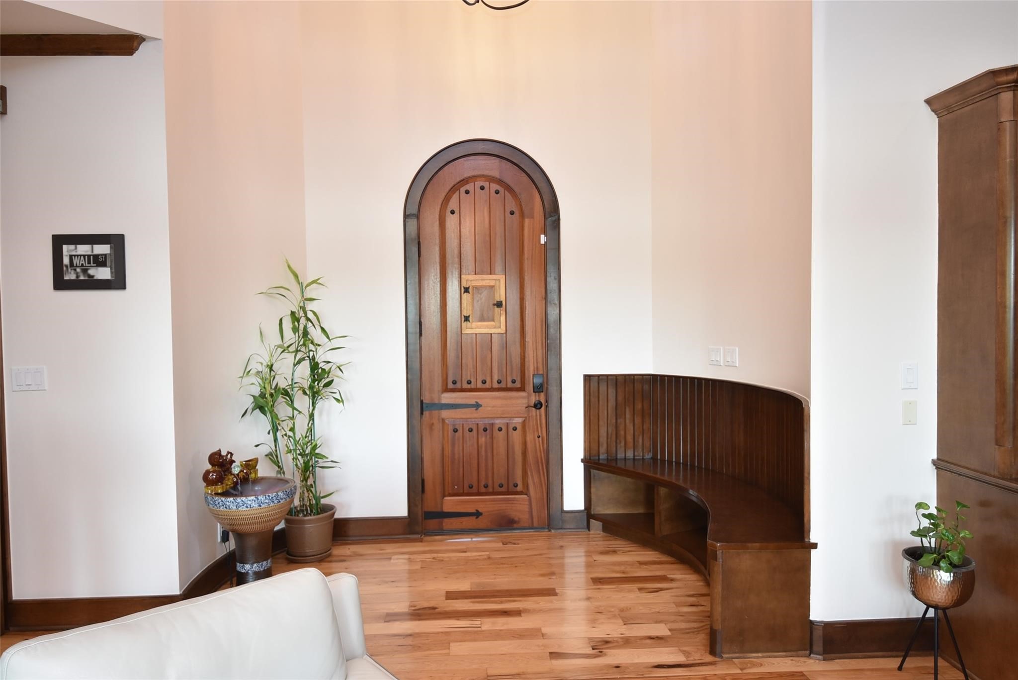 825 Grubbs Road Sealy, TX 77474 - Photo 7 of 47 This inviting entryway features a charming wooden arched door, warm hardwood floors, and a built-in curved wooden bench. Accents include potted plants and a decorative wall piece, creating a welcoming atmosphere.