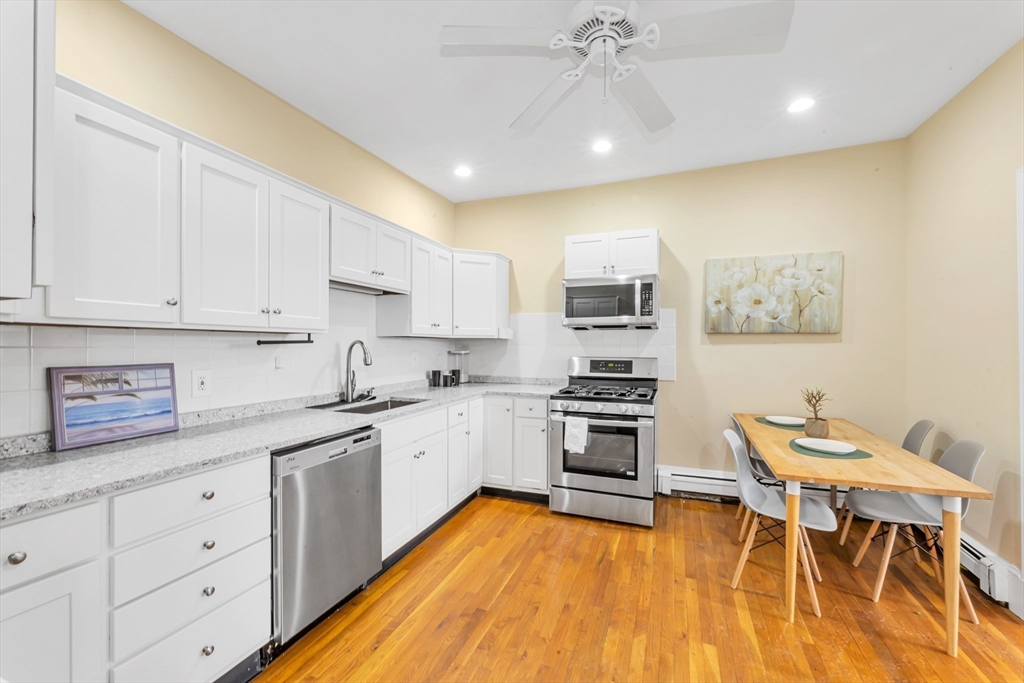 122 Day Street, Unit 3 Boston, MA 02130 - Photo 7 of 14 a kitchen with stainless steel appliances kitchen island granite countertop a stove a sink and white cabinets with wooden floor
