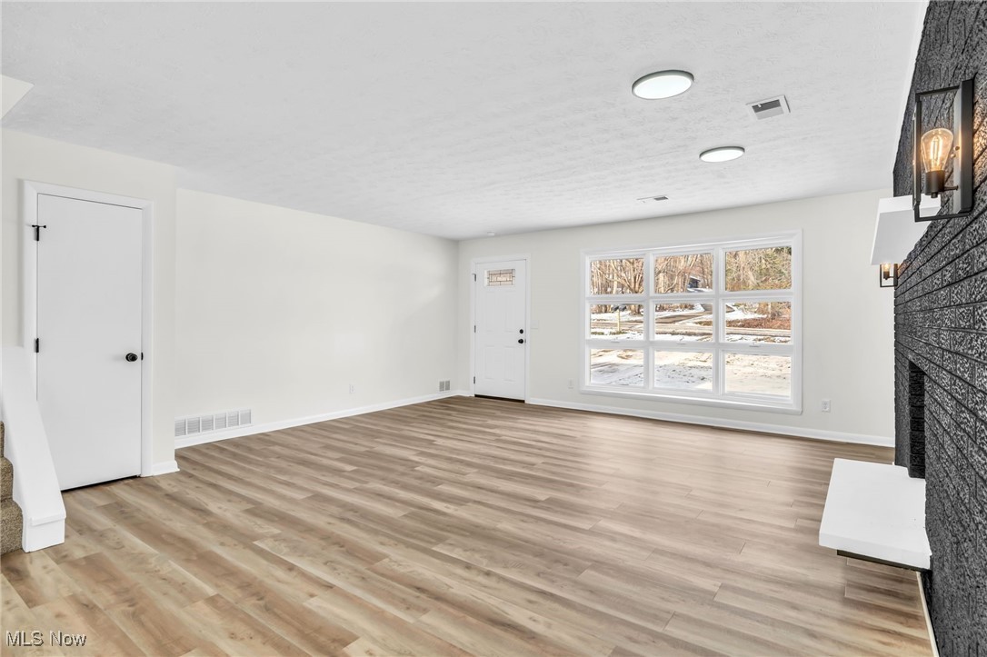 Unfurnished living room with a fireplace with raised hearth, light wood finished floors, and a textured ceiling