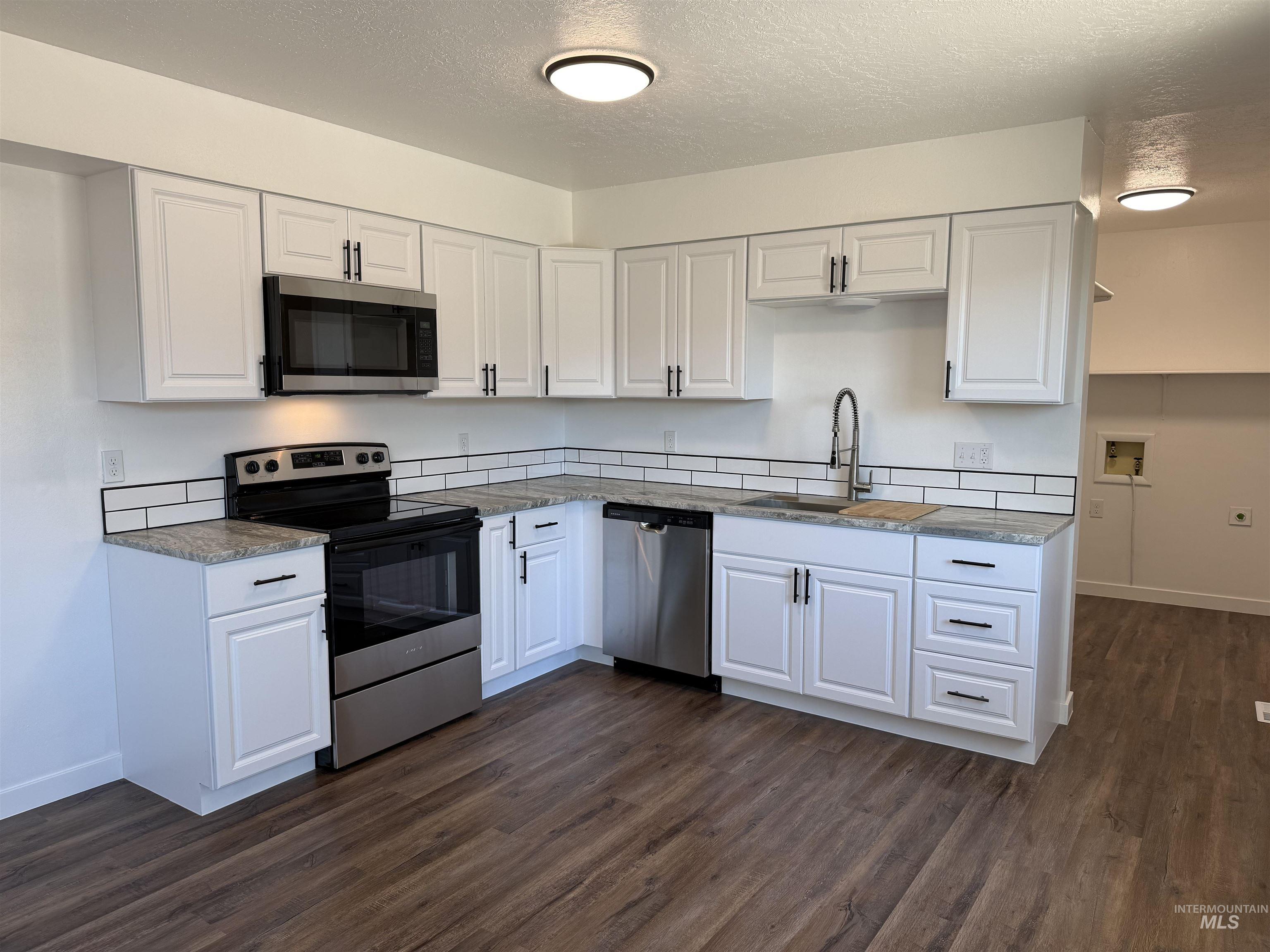 709 Locust Street Kimberly, ID 83341 - Photo 3 of 13 Kitchen with stainless steel appliances, a textured ceiling, dark wood-type flooring, white cabinetry, and light stone counters