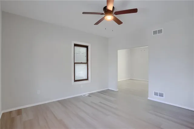 an empty room with wooden floor ceiling fan and windows
