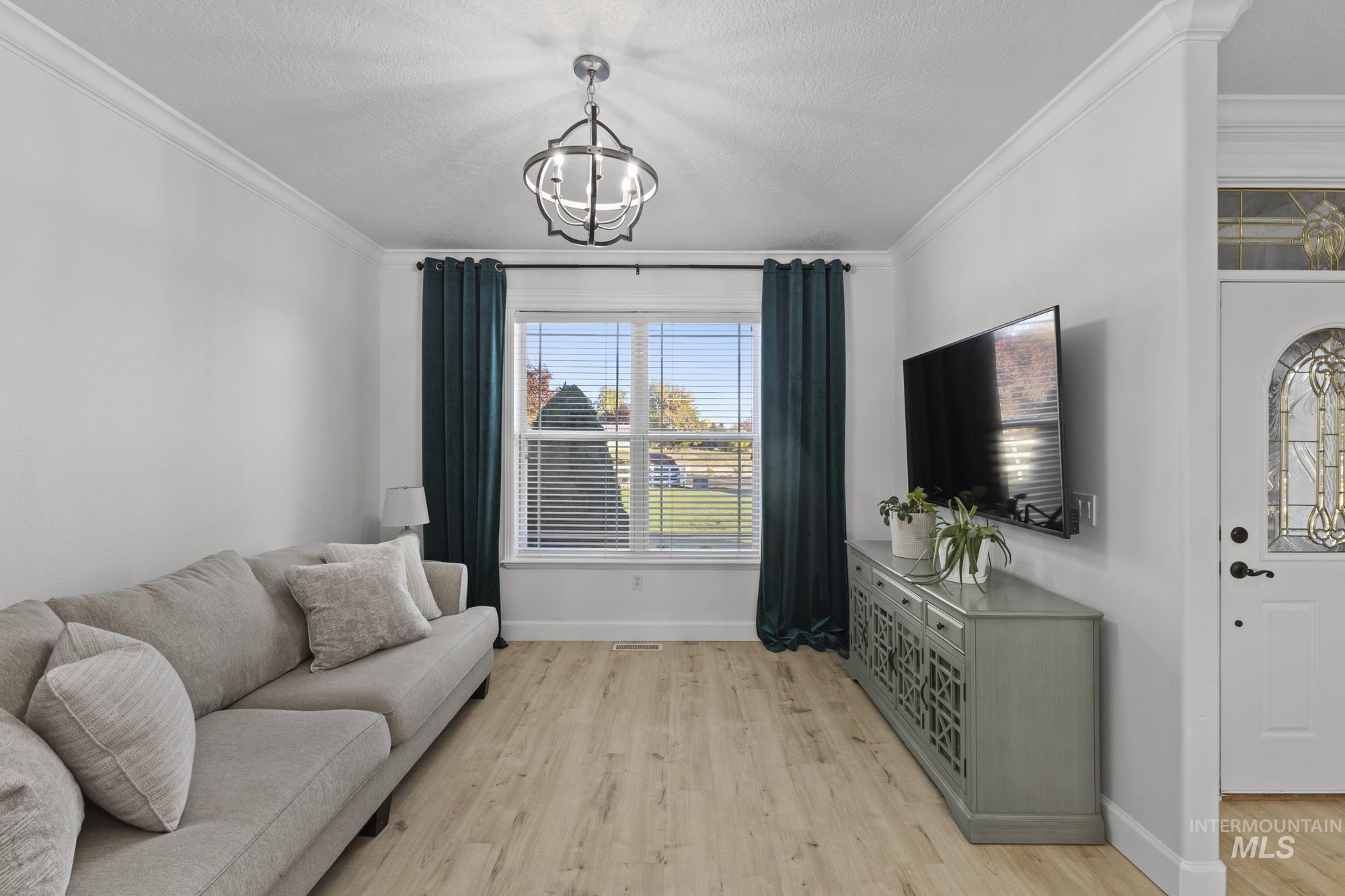 14820 Worden Way Caldwell, ID 83607 - Photo 11 of 44 Living room featuring light wood-style flooring, a textured ceiling, ornamental molding, and hanging lights
