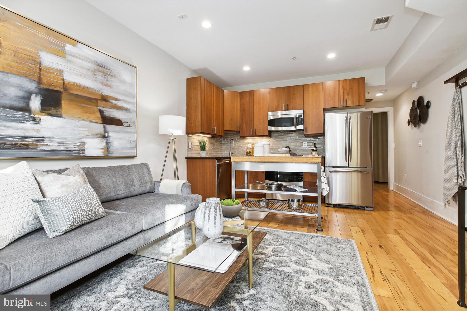 a living room with stainless steel appliances furniture a rug and a kitchen view