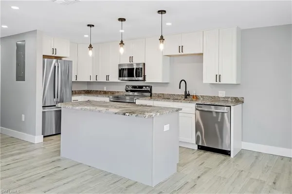 a kitchen with stainless steel appliances granite countertop a refrigerator a stove a sink dishwasher and white cabinets with wooden floor