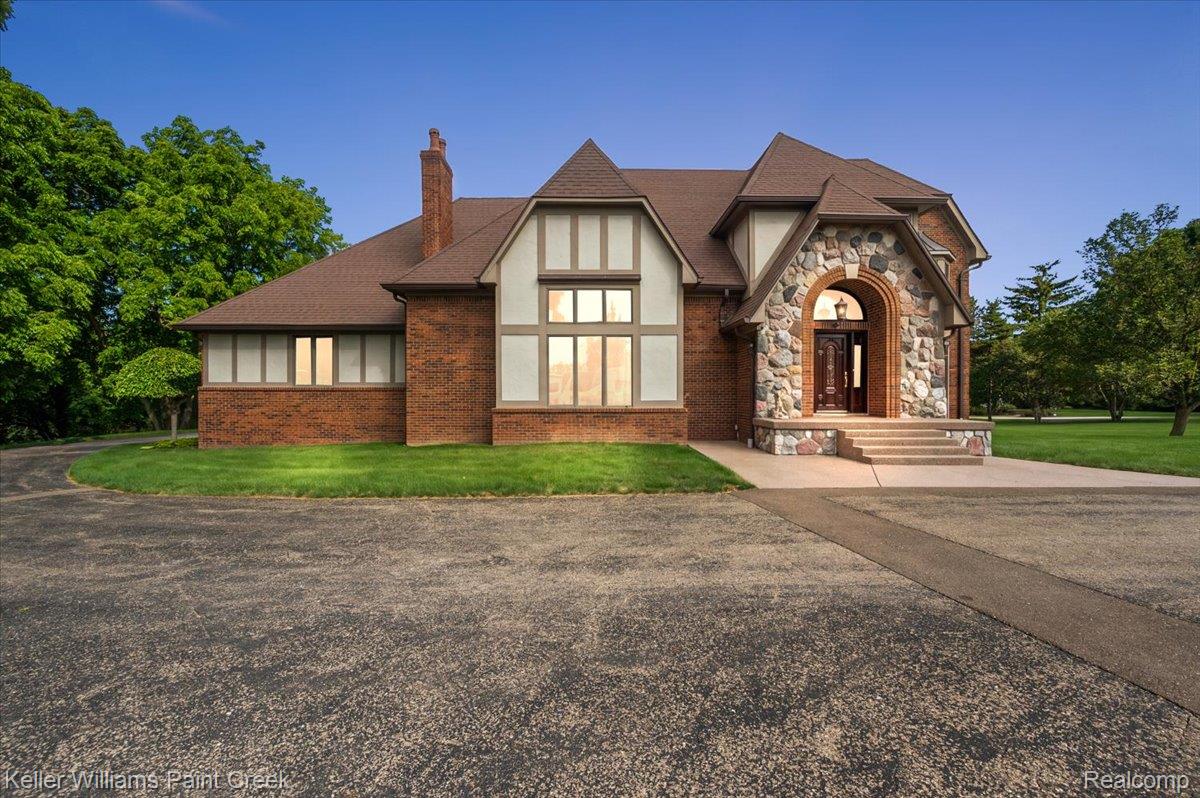Tudor-style residence featuring a prominent stone archway entry, multi-pane windows, and a brick exterior with stucco and timber accents