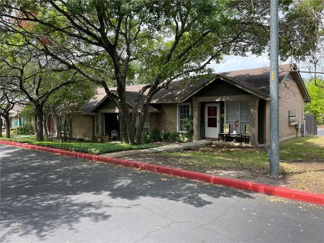 a view of a house with small yard plants and a large tree