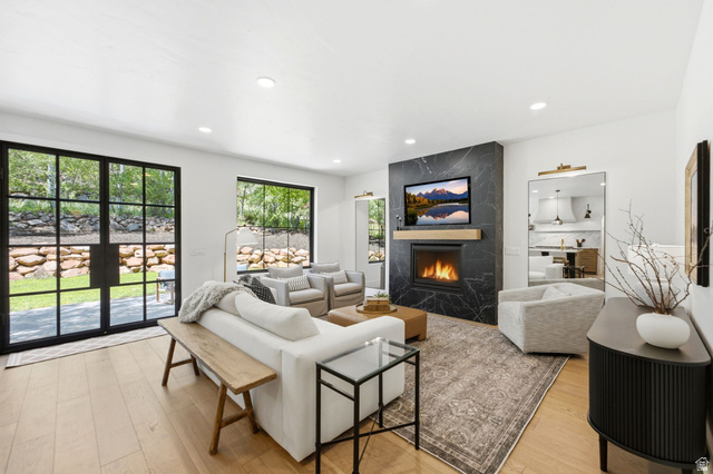3027 Homestead Road Park City, UT 84098 - Photo 12 of 62 Spacious living area featuring a sleek fireplace with a black stone surround and wood mantel, large black-framed glass doors, light wood-finish flooring, recessed lighting, and a patterned area rug