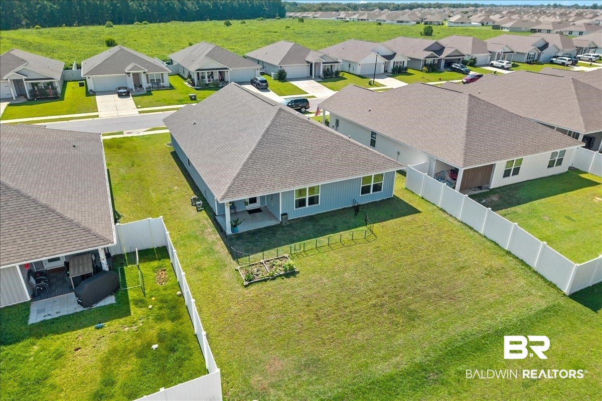 23641 Unbridled Loop Daphne, AL 36526 - Photo 32 of 40 Aerial perspective showcasing a light blue single-story home with a covered patio, a spacious fenced backyard featuring a garden bed, and a gravel-colored shingled roof