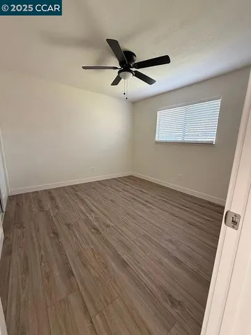 an empty room with wooden floor a ceiling fan and windows
