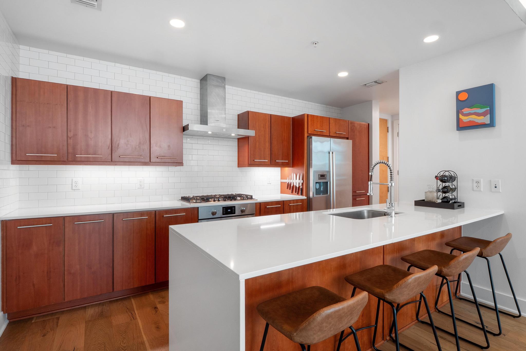 Kitchen with wall chimney range hood, a sink, a kitchen breakfast bar, stainless steel appliances, and a peninsula