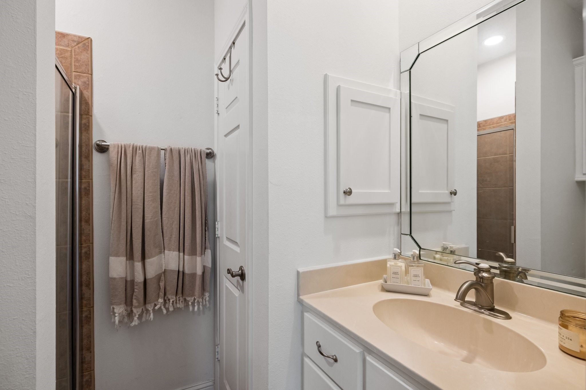 34310 High Point Drive Magnolia, TX 77355 - Photo 29 of 48 This bathroom features a modern design with a tiled shower, cream countertop, and a stylish mirror. It includes white cabinetry and a towel rack, providing a clean and functional space.