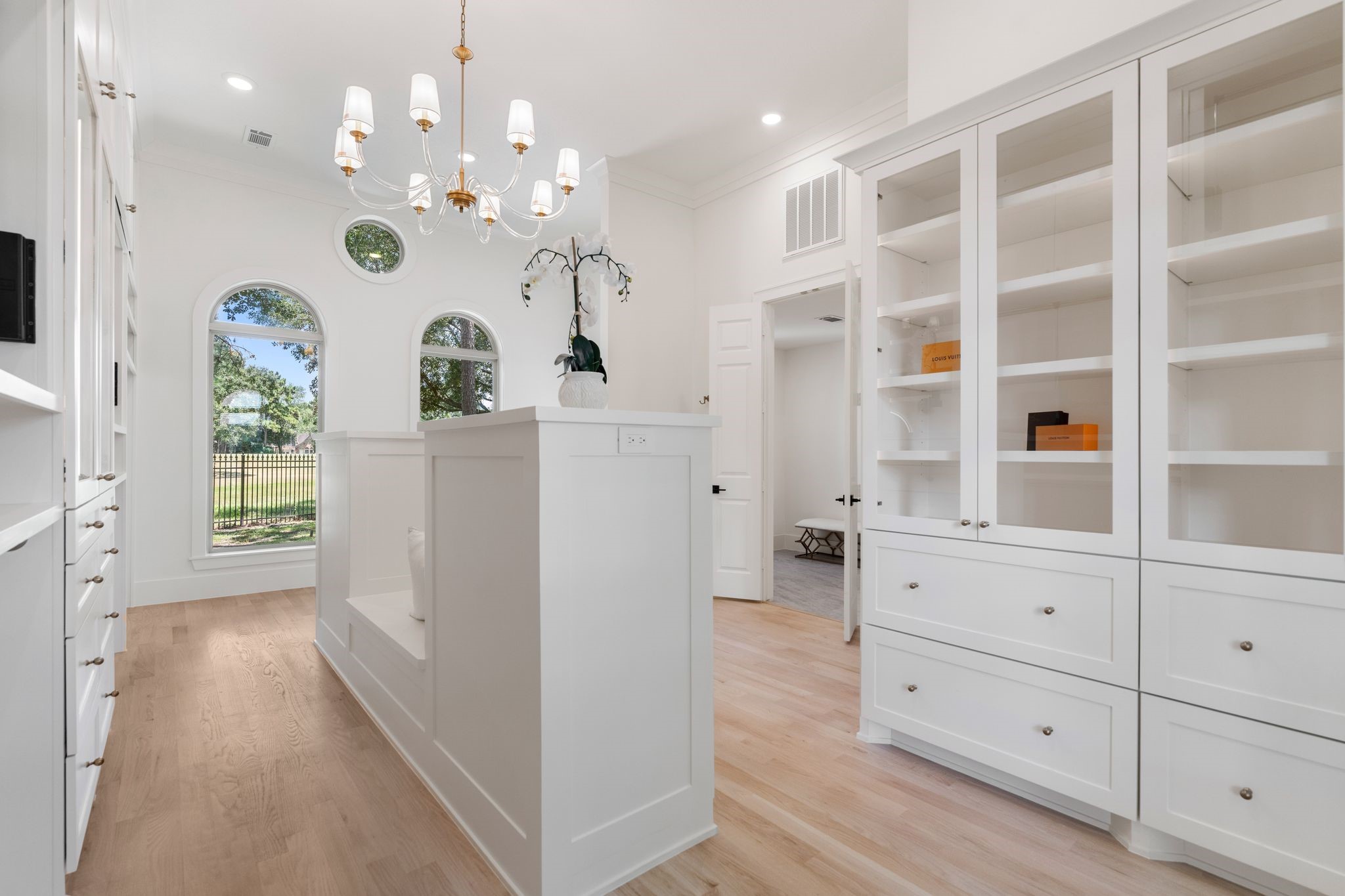 31 Hollymead Drive Spring, TX 77381 - Photo 28 of 50 This bright, elegant room features built-in white cabinetry with glass doors, arched windows offering natural light and scenic views, and a stylish chandelier. The hardwood floors and open design create a spacious and inviting atmosphere.