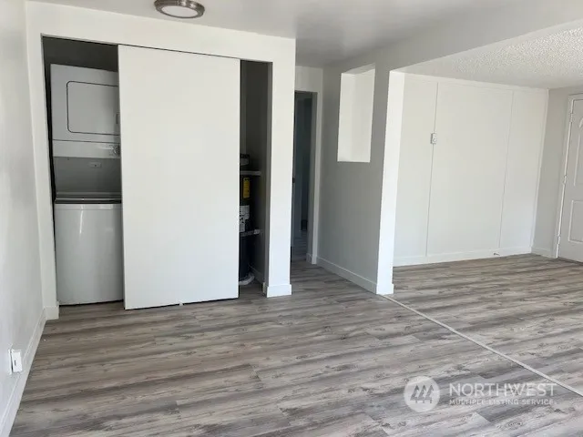 a view of an empty room with wooden floor and a kitchen
