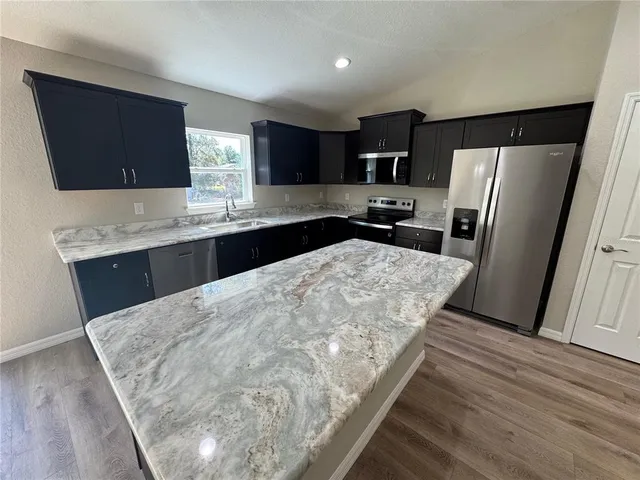 a kitchen with stainless steel appliances kitchen island granite countertop a refrigerator a sink a stove a microwave a counter top and oven with wooden floor