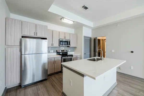 a kitchen with kitchen island a refrigerator a stove a sink and white cabinets with wooden floor