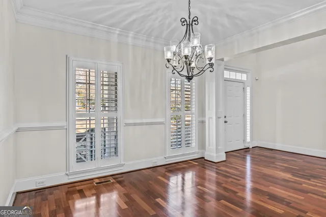 an empty room with wooden floor chandelier and windows