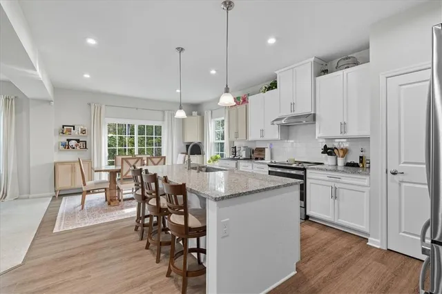 a kitchen with stainless steel appliances granite countertop a stove a refrigerator a kitchen island a dining table and chairs with wooden floor