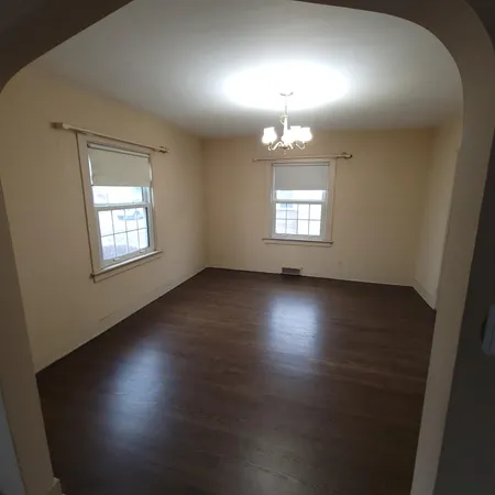 an empty room with wooden floor chandelier and windows