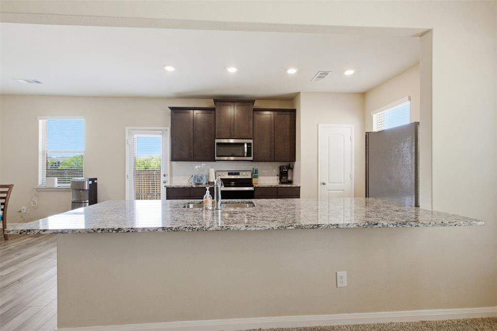 292 Wandering Stream Way Princeton, TX 75407 - Photo 11 of 40 Kitchen featuring dark wood finish cabinetry, light stone countertops, stainless steel appliances, recessed lighting, and tasteful backsplash