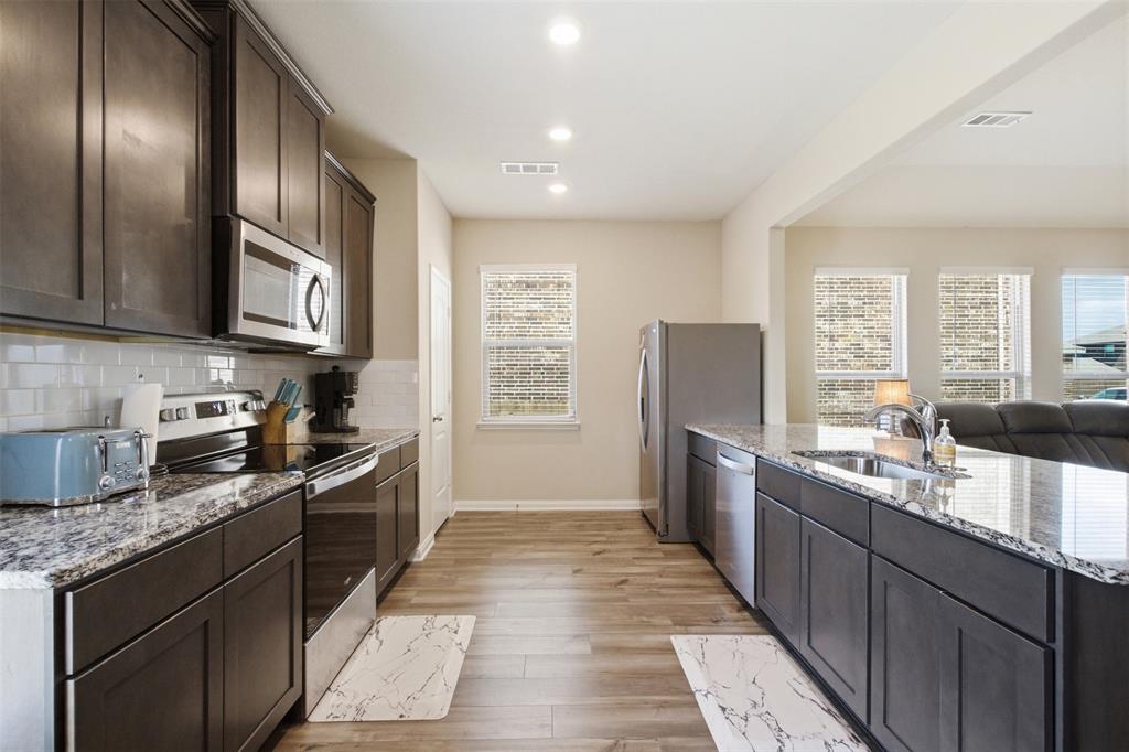 292 Wandering Stream Way Princeton, TX 75407 - Photo 39 of 40 Kitchen featuring stainless steel appliances, dark wood finish cabinetry, light wood-style floors, open floor plan, and light stone countertops