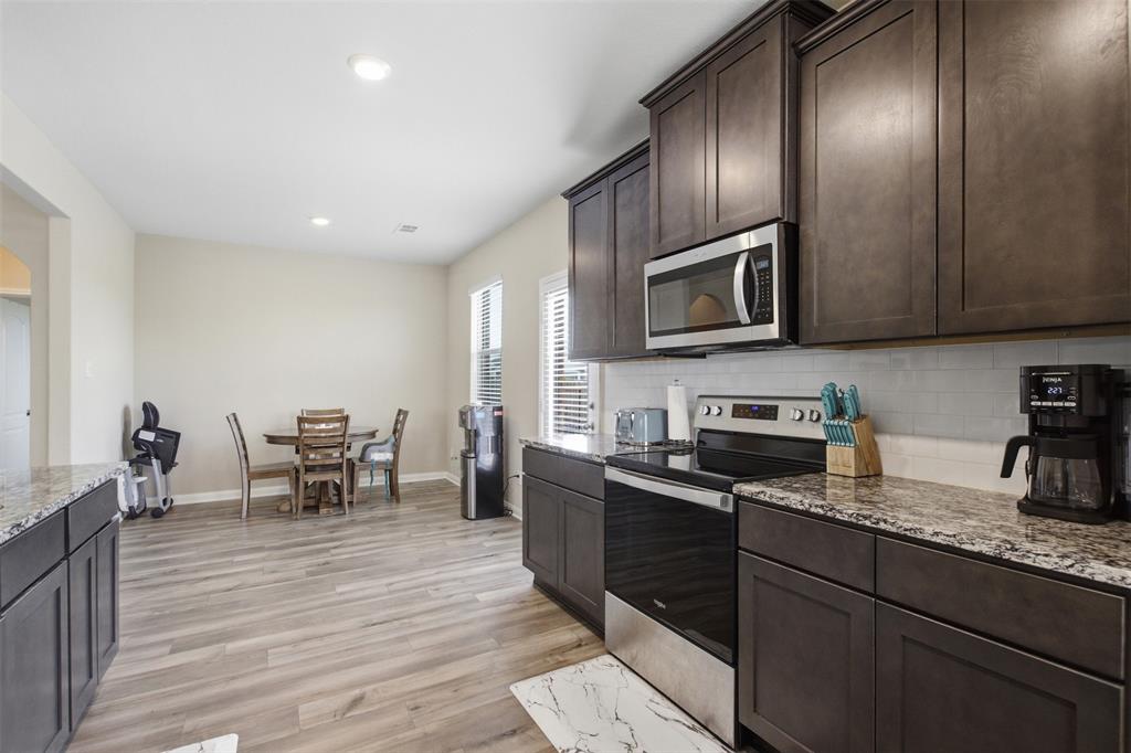 292 Wandering Stream Way Princeton, TX 75407 - Photo 13 of 40 Kitchen with dark wood finish cabinets, stainless steel appliances, light stone counters, light wood-type flooring, and backsplash