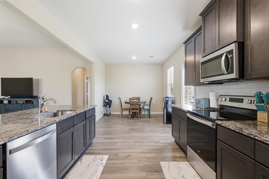 292 Wandering Stream Way Princeton, TX 75407 - Photo 14 of 40 Kitchen featuring stainless steel appliances, dark wood finish cabinets, dark stone counters, arched walkways, and light wood-type flooring