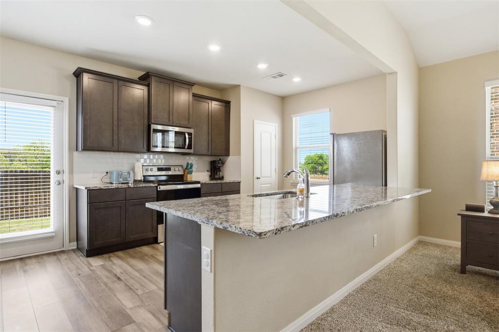 292 Wandering Stream Way Princeton, TX 75407 - Photo 10 of 40 Kitchen with dark wood finish cabinets, stainless steel appliances, light stone counters, a kitchen island with sink, and decorative backsplash