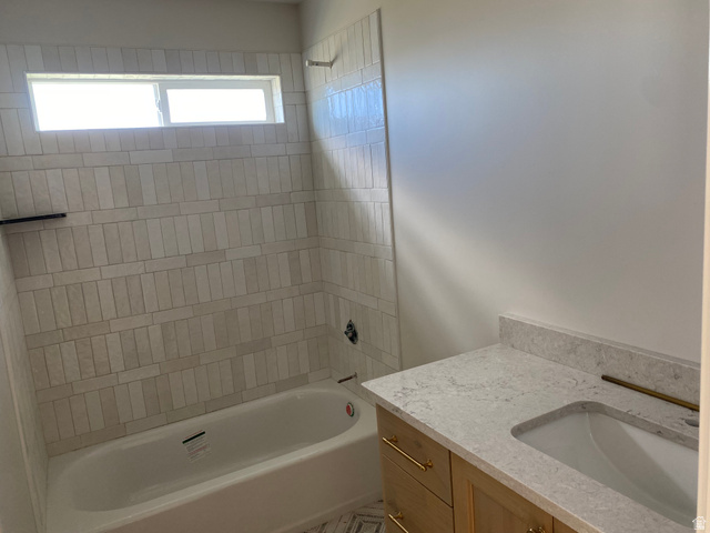 4676 West 75 North, Unit 401 West Point, UT 84015 - Photo 13 of 17 Bathroom featuring a built-in bathtub with subway tile surround, integrated window, light wood-finish vanity with gold-tone hardware, and a stone countertop with undermount sink