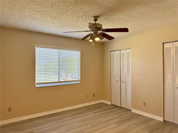 a view of an empty room with wooden floor and a ceiling fan