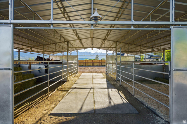 681 Island Road Morgan, UT 84050 - Photo 25 of 49 Covered equestrian facility featuring a metal roof structure, open-air stalls with metal bar fencing, a central concrete walkway, and overhead lighting fixtures