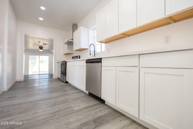 a kitchen with stainless steel appliances granite countertop a refrigerator a sink dishwasher a stove and white countertops with wooden floor