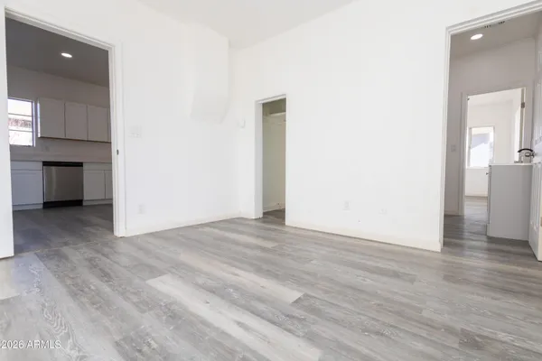 a view of an empty room with wooden floor and a kitchen