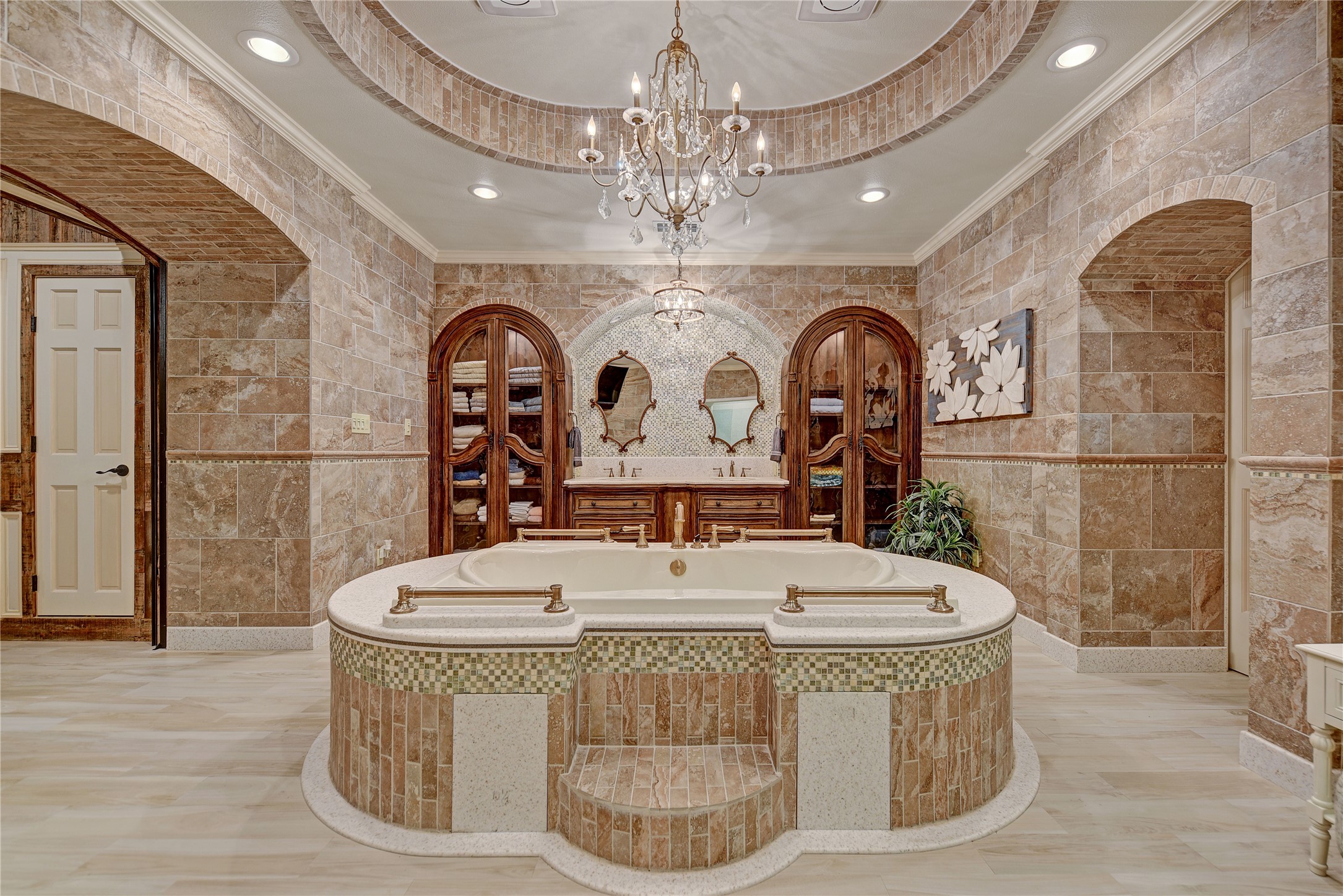 9950 Palestine Road Brenham, TX 77833 - Photo 17 of 49 The primary bathroom, enclosed by leaded glass pocket doors, features dual sinks anchored by built-in custom furniture and framed mirrors surrounded by mosaic tile, a garden tub with vertically laid stone surround with mosiac tile inserts, a designer chandelier, and huge his/her walk-in closets. This is one of two bathrooms located in the primary suite.