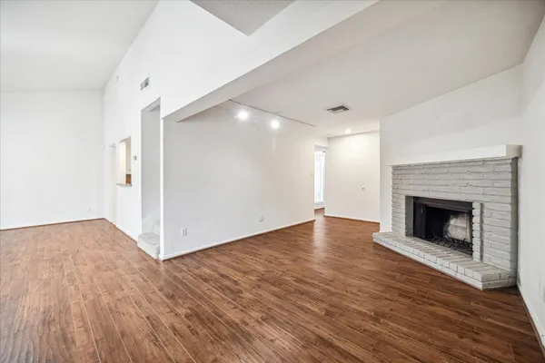 a view of an empty room with wooden floor fireplace and a window