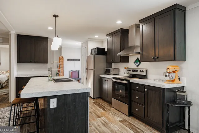 a kitchen with stainless steel appliances kitchen island granite countertop a refrigerator a sink dishwasher a stove and white cabinets with wooden floor