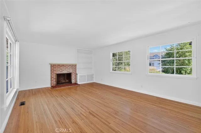 an empty room with wooden floor fireplace and windows
