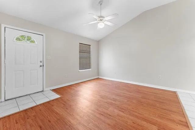 an empty room with wooden floor ceiling fan and windows