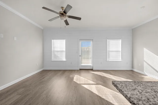 an empty room with wooden floor fan and windows