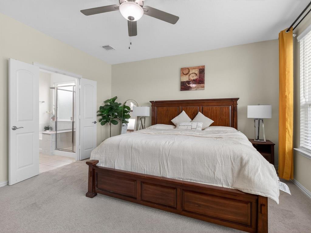 636 Corner Post Path Celina, TX 75009 - Photo 17 of 40 Carpeted bedroom featuring a ceiling fan with integrated lighting, window with blinds, and white double doors opening to a bathroom with a glass-enclosed shower and separate soaking tub