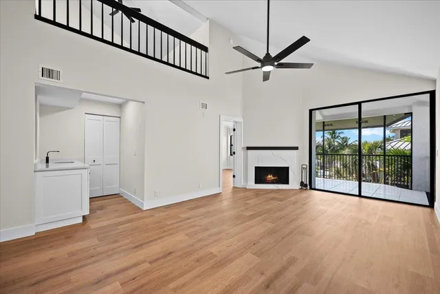 a view of a livingroom with wooden floor a fireplace a ceiling fan and windows