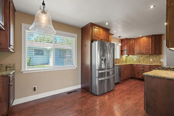 a kitchen with stainless steel appliances granite countertop a stove a sink dishwasher and a refrigerator with wooden floor