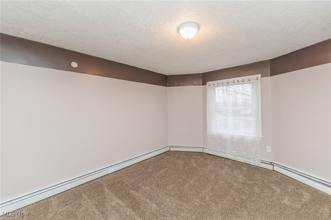 3181 Warren Road Cleveland, OH 44111 - Photo 16 of 28 Empty room featuring a textured ceiling, carpet flooring, and a baseboard heating unit